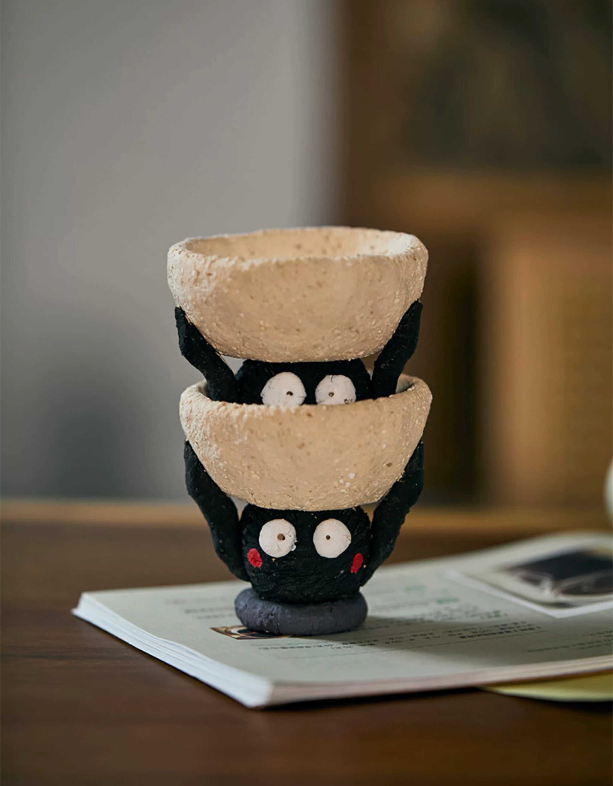 Two handmade ceramic Soot Spirit candle holders stacked together, showing their playful black faces and textured cream bowls.
