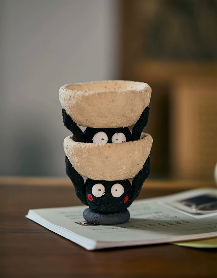 Two handmade ceramic Soot Spirit candle holders stacked together, showing their playful black faces and textured cream bowls.