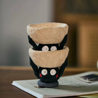 Two handmade ceramic Soot Spirit candle holders stacked together, showing their playful black faces and textured cream bowls.