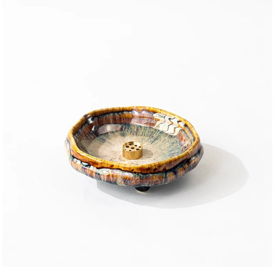 Handmade wabi-sabi ceramic incense holder with warm brown crackle glaze and a brass incense insert on a white background.