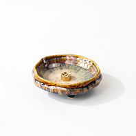 Handmade wabi-sabi ceramic incense holder with warm brown crackle glaze and a brass incense insert on a white background.