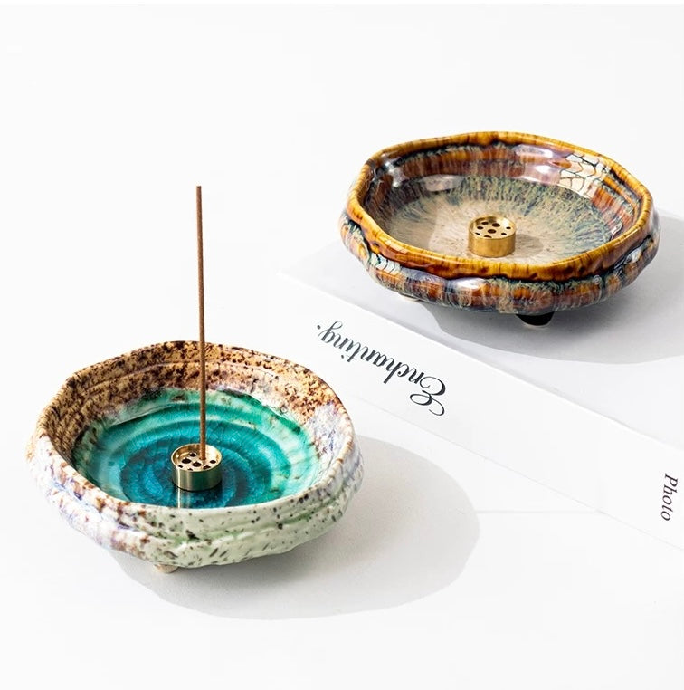 Two handmade wabi-sabi ceramic incense holders, one green and one brown, each with a brass incense insert and incense stick on a white background.
