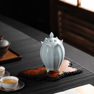 White lotus shaped electric ceramic incense burner displayed on a decorative tray beside tea cups in a sunlit tea room
