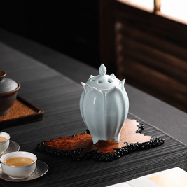 White lotus shaped electric ceramic incense burner displayed on a decorative tray beside tea cups in a sunlit tea room