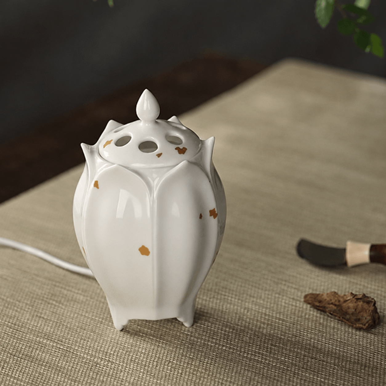 White lotus shaped electric ceramic incense burner with gold flecks displayed beside incense wood and a small incense tool