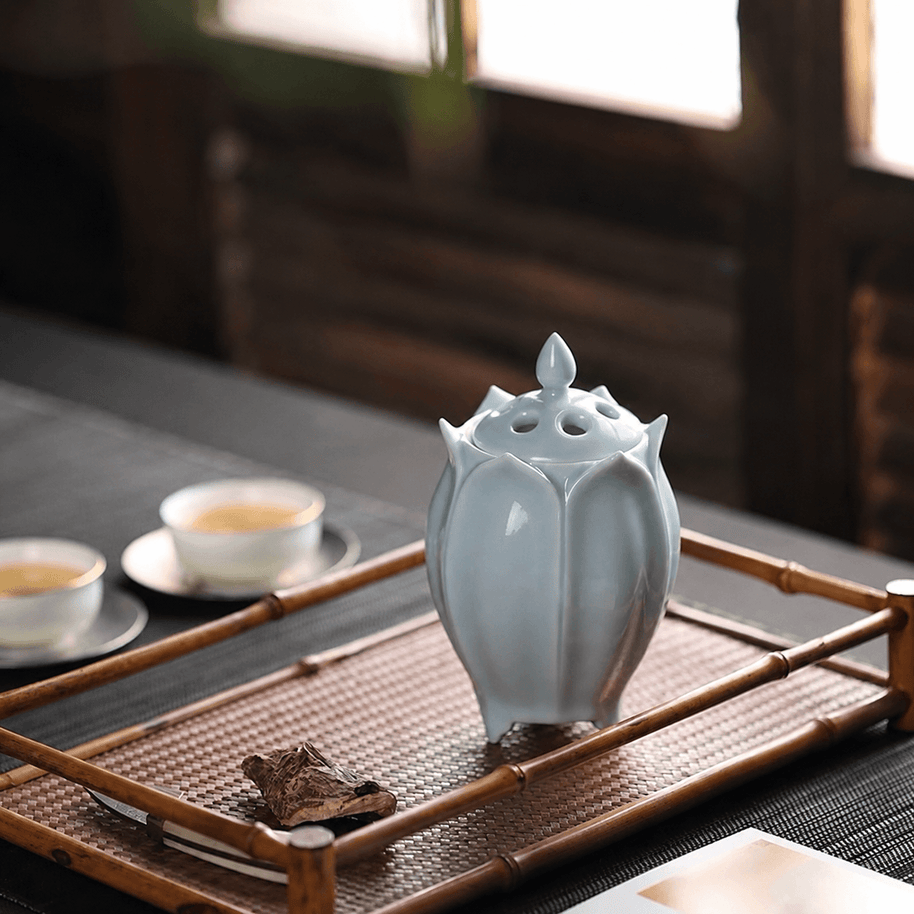 White lotus shaped electric ceramic incense burner displayed on a bamboo tray beside tea cups and incense wood