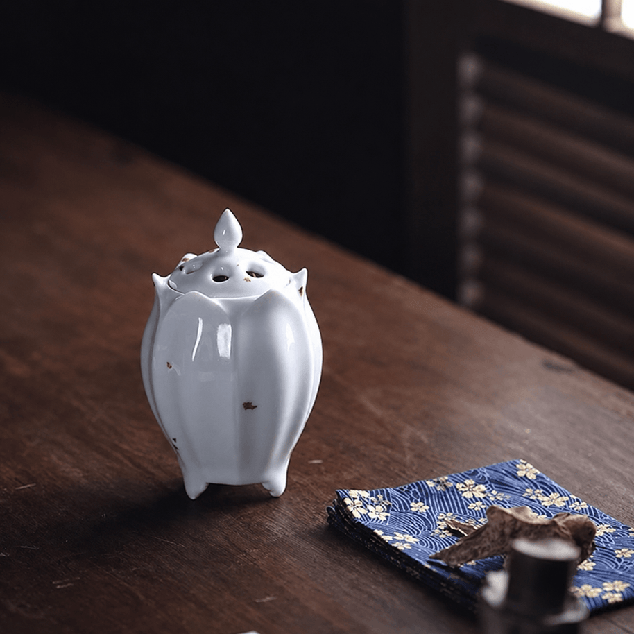 White lotus shaped electric ceramic incense burner with gold flecks displayed on a wooden table beside incense materials