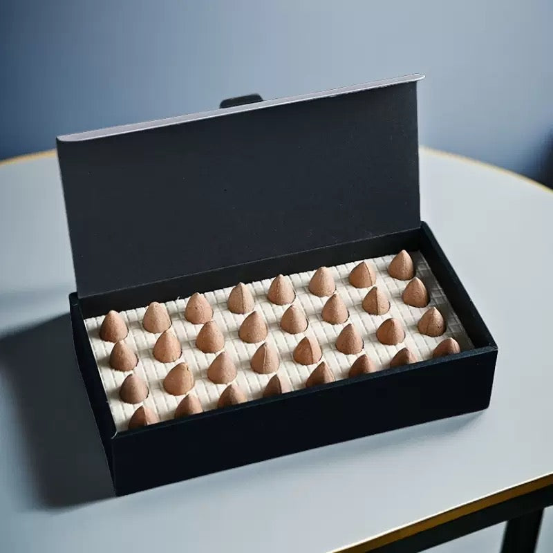 Open black box filled with wormwood backflow incense cones arranged in rows on a table for backflow waterfall incense burner