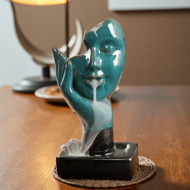Front view of Abstract Face Backflow Incense Burner with turquoise glaze and flowing smoke.