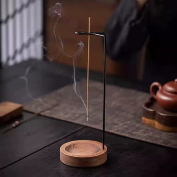 Backflow incense burner with hanging stick holder and wooden base placed on a tea table with smoke rising