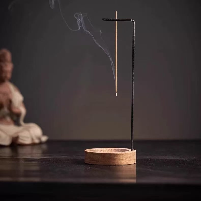 Backflow incense burner with wooden base and hanging stick holder on a dark table, incense smoke rising, Buddha statue blurred in background