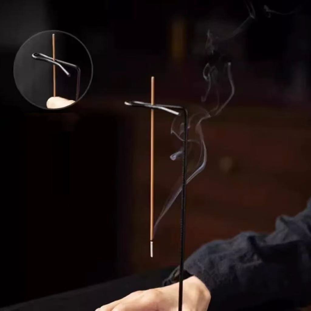 Close-up of a backflow incense burner with wooden base and hanging stick holder, swirling smoke, circular detail inset, warm background, hand partially visible