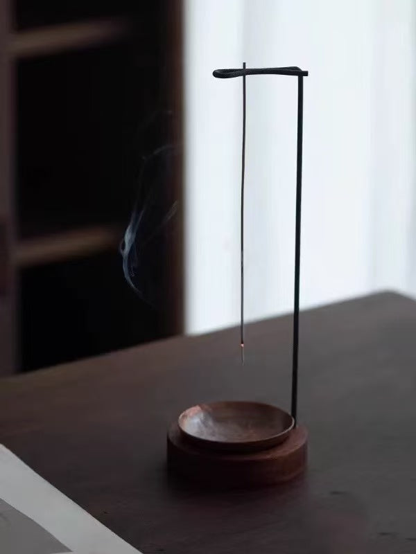 Backflow incense burner with wooden base and hanging stick holder in soft window light on a tabletop, minimal scene, faint smoke