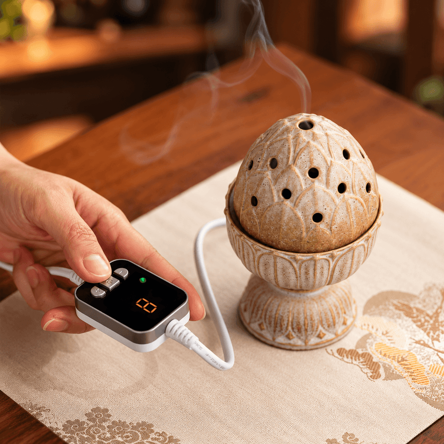 Hand operating the digital timer beside a beige lotus electric incense burner, with smoke rising through its perforated lid.