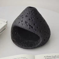Natural black stone incense burner with a volcanic texture, displayed on an open book and white surface in a minimalist setting
