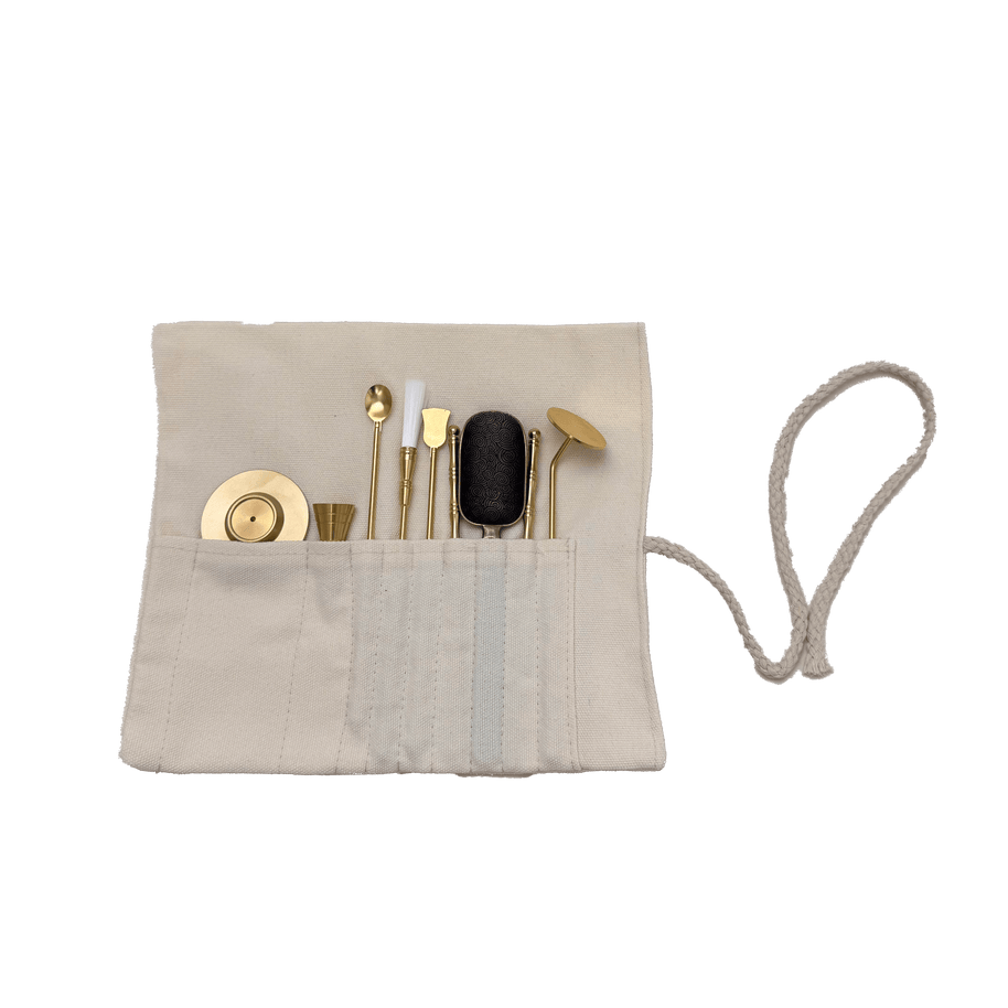 Top view of brass incense tool kit neatly arranged in cotton storage wrap, showing spatulas, tongs, press, and spoon tools on transparent background
