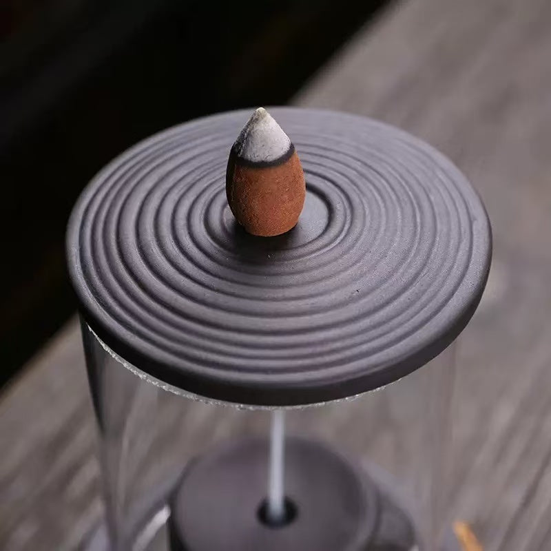 Close-up of a backflow incense cone placed on a circular metal lid with concentric ring design.