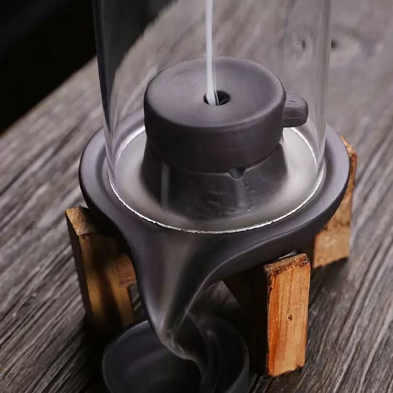 Close-up of smoke flowing through a glass backflow incense burner with wooden stand and ceramic core.