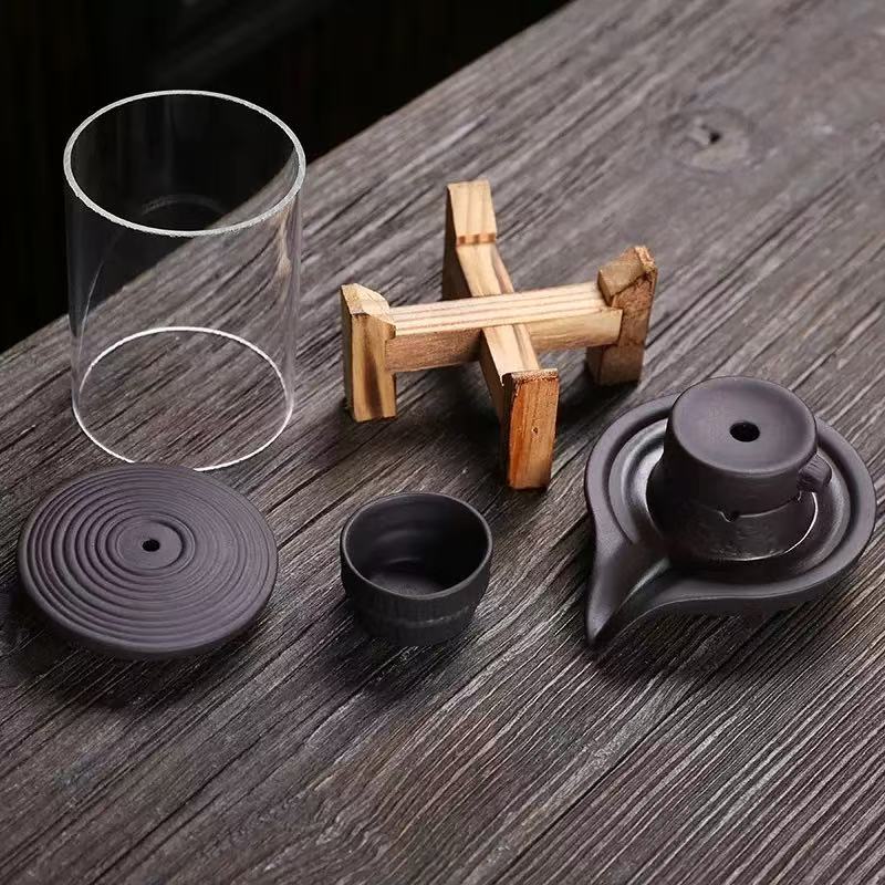 Disassembled glass backflow incense burner with wooden base, ceramic parts, and lid shown on a wooden surface.