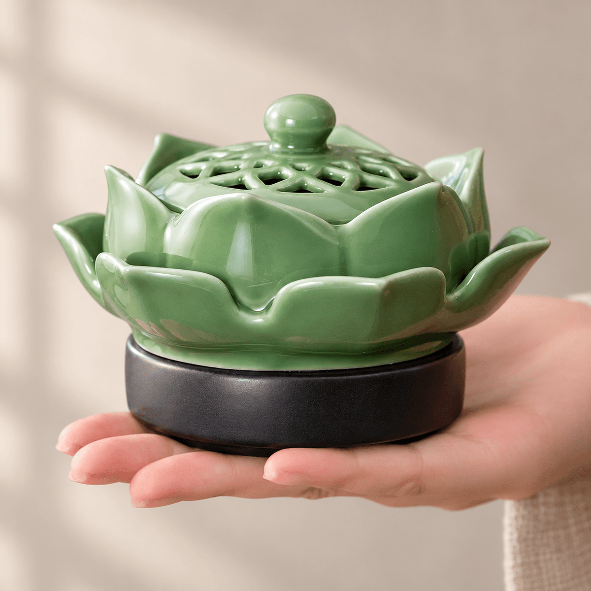 Green ceramic lotus electric incense burner resting on an open palm to show its size and layered petal design.