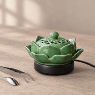 Green lotus electric incense burner with a decorative ceramic lid and black base, beside a metal spoon and tweezers.