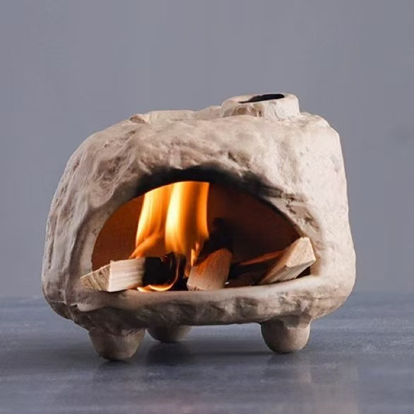 Handmade ceramic incense burner with raised legs and textured surface, glowing inside with burning wood incense pieces for calming aromatherapy or ritual use
