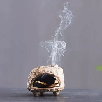 Handmade ceramic incense burner with gentle diffusion groove, releasing spiral smoke from palo santo wood in a minimalist dark background