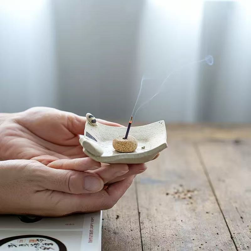 Handmade ceramic incense holder with cat figurine, shown in hand with incense stick burning, artisanal incense burner for yoga, meditation, and home decor.
