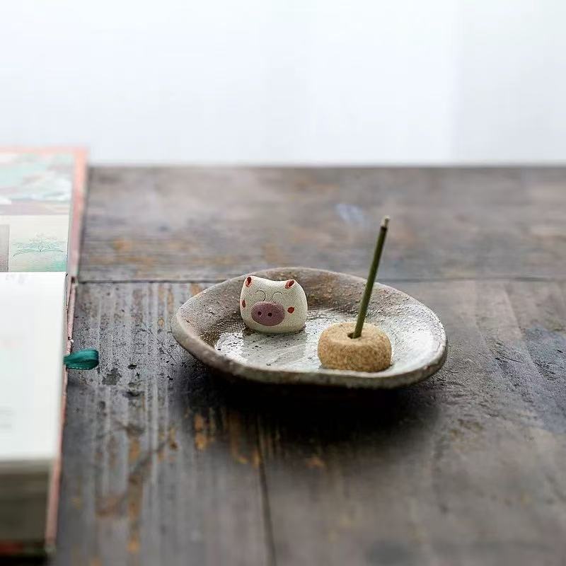 Handmade ceramic incense holder with pig figurine, incense stick burning, artisanal incense burner for relaxation, aromatherapy, and home decoration.
