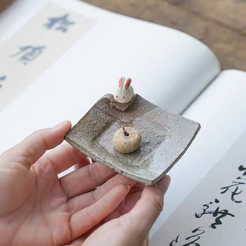 Handmade ceramic incense holder with rabbit figurine, shown in hand for size reference, artisanal incense burner for meditation and home decor.
