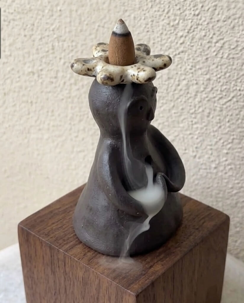 Close up of a handmade ceramic backflow incense burner with speckled flower crown and gentle smoke flow.