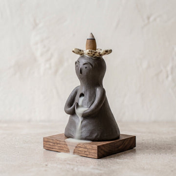Handmade ceramic backflow incense burner displayed on a wooden base with flowing smoke for meditation and home decor.