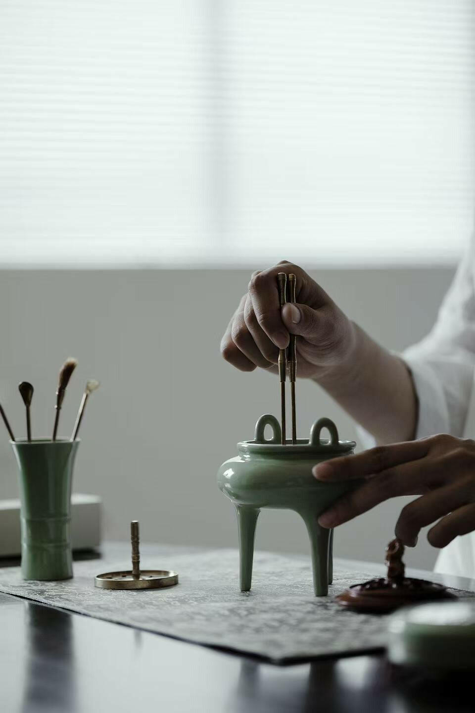 Demonstration of using celadon incense burner from the Incense Bath Ceremony Set, with person placing incense tools into the burner on a tabletop