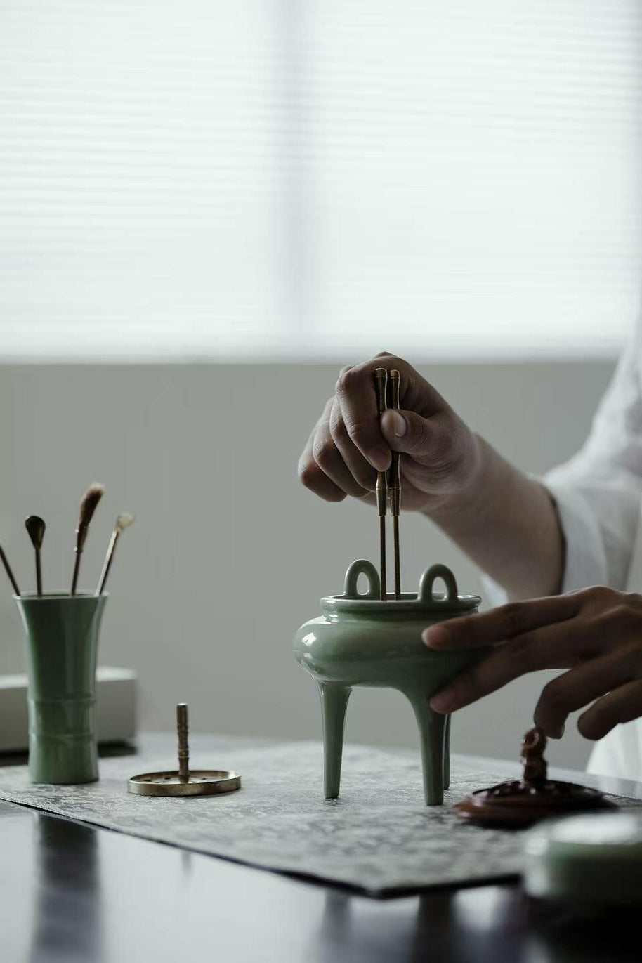 Demonstration of using celadon incense burner from the Incense Bath Ceremony Set, with person placing incense tools into the burner on a tabletop