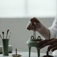 Demonstration of using celadon incense burner from the Incense Bath Ceremony Set, with person placing incense tools into the burner on a tabletop