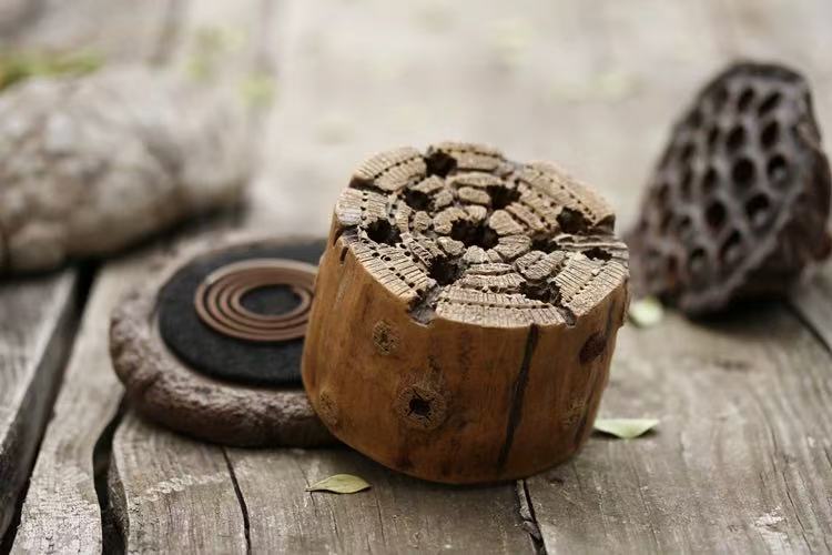 Vintage wood-stump incense burner on aged wooden table with incense coil and dried lotus pod
