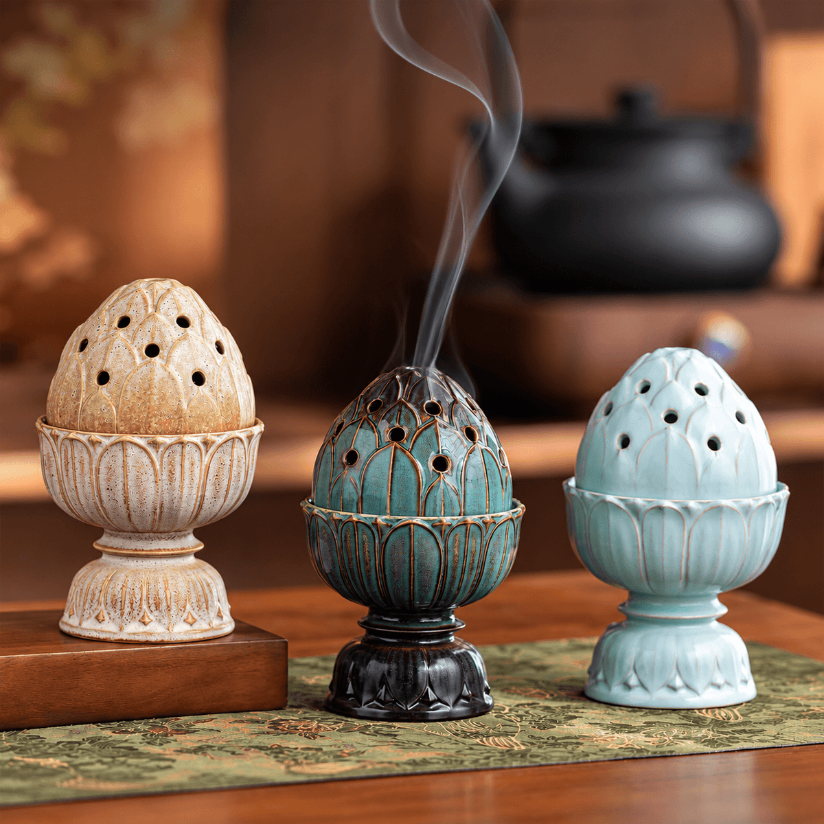 Beige, teal and pale blue lotus ceramic incense burners displayed together, with smoke rising from the teal burner.