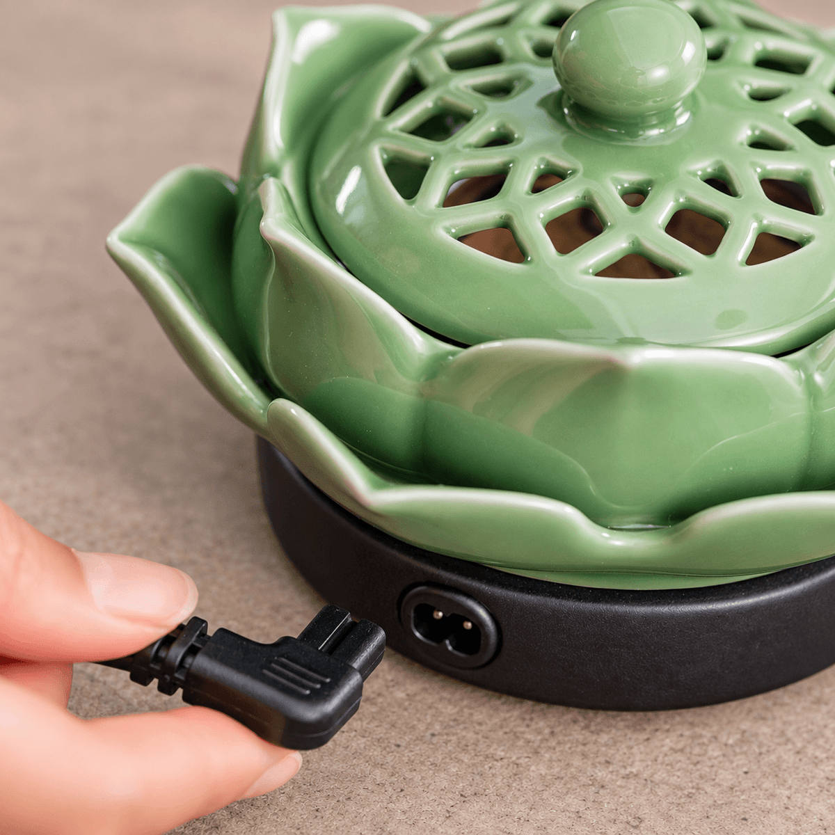 Close view of the detachable power cord connector and socket on the black base of the green lotus electric incense burner.