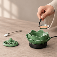 A hand uses tweezers to lift a metal dish filled with incense powder above the open lotus electric incense burner.