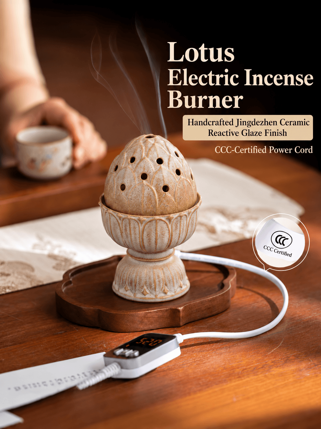 Lotus ceramic electric incense burner releasing wisps of smoke on a wooden tray beside a teacup, with its digital controller.