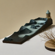 Close-up of Mountain Mist wooden incense holder with backflow cone on raised platform, sculpted to resemble layered peaks, styled on neutral background