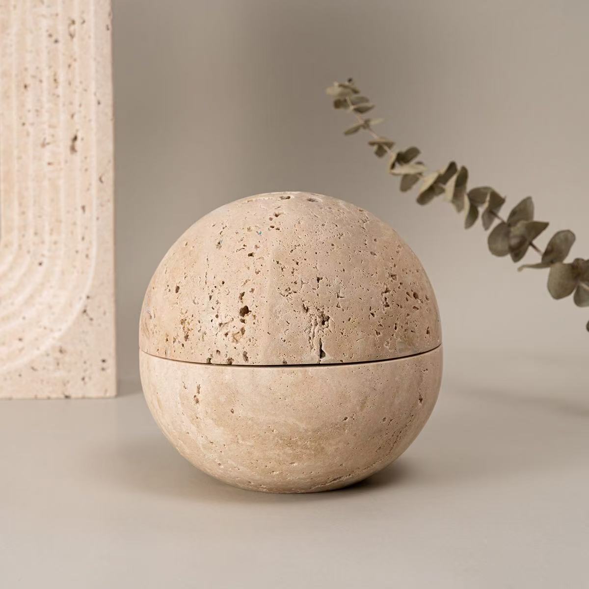 Closed natural travertine incense burner in full sphere shape placed on minimal background with eucalyptus branch decor