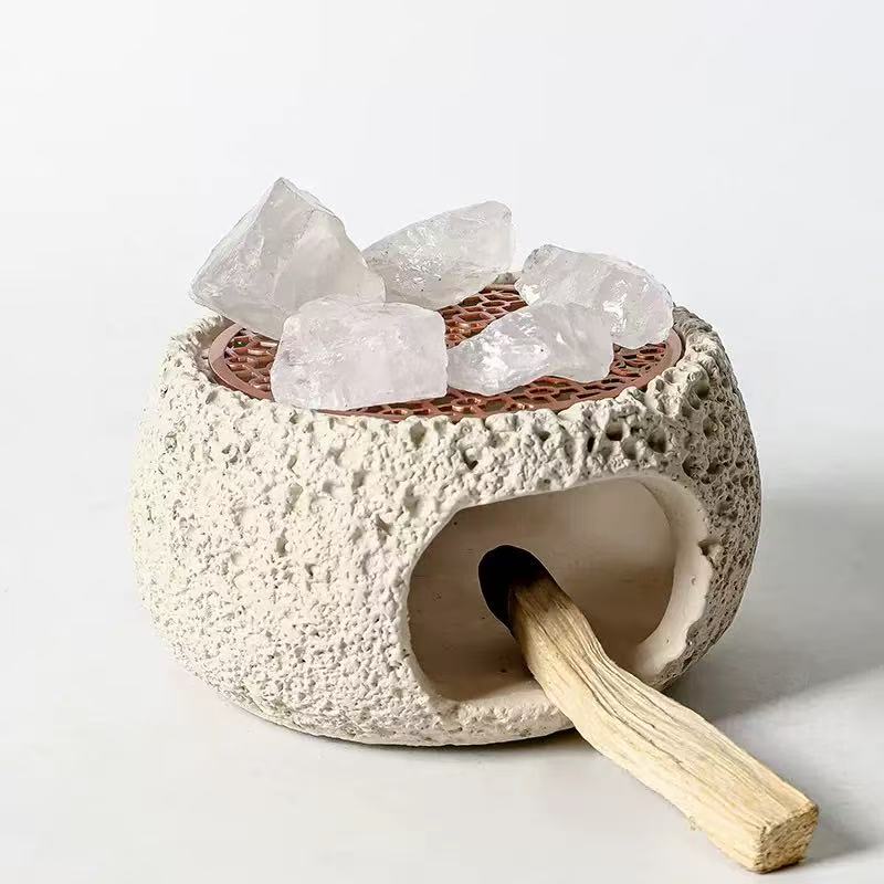 Off-white cement incense burner with raw quartz crystals and rosewood grate, used for burning palo santo sticks in spiritual cleansing rituals
