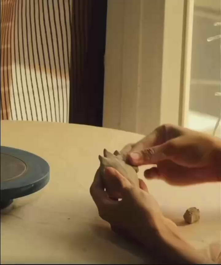 Short video of an artisan sculpting the clay flame incense holder and tray by hand on a workbench.