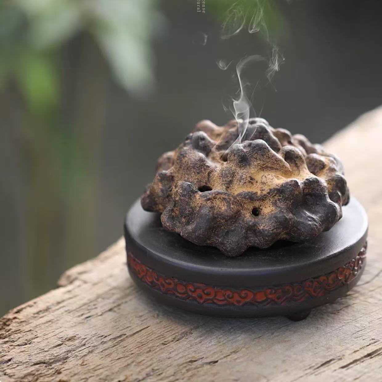Rock-form purple clay incense burner emitting smoke on wooden surface with green nature background
