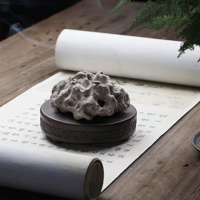 Rock-form purple clay incense burner with smoke, placed on calligraphy scroll beside ceramic brush holder
