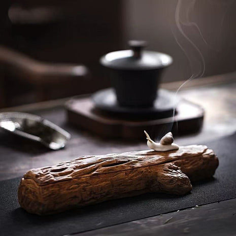 Snail-shaped ceramic incense burner on a rustic wooden incense base, surrounded by a traditional tea set