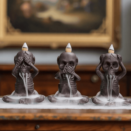 Set of three skeleton-shaped backflow incense burners in "hear no evil, see no evil, speak no evil" poses with smoke flowing from their mouths.