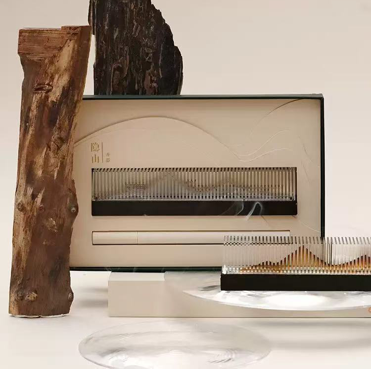 Transparent landscape stick incense burner set featuring an acrylic holder and wooden base, displayed in front of a sculpted wood element and