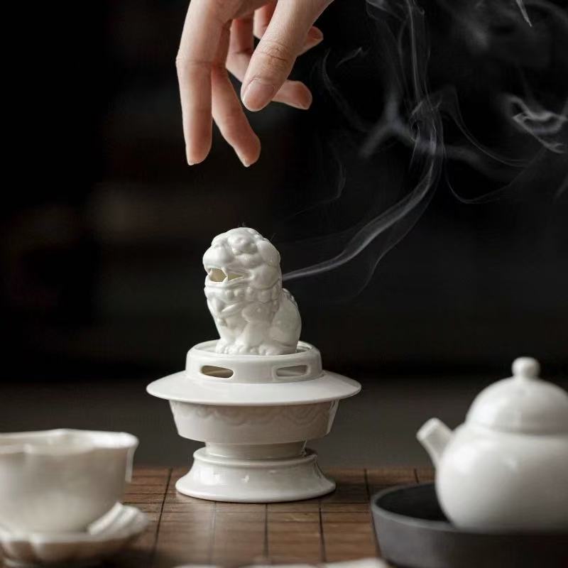 Close-up of white ceramic guardian lion incense burner with smoke curling from the mouth, placed on a wooden tea table

